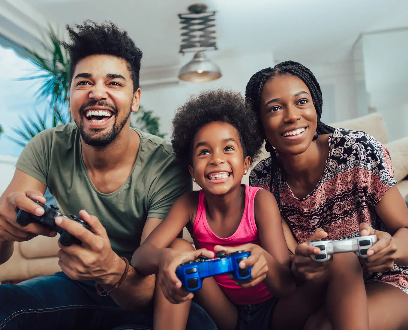 Smiling family sitting together on a couch playing video games in a bright, comfortable living room, representing clean, healthy indoor air quality for a safe and enjoyable home environment.
