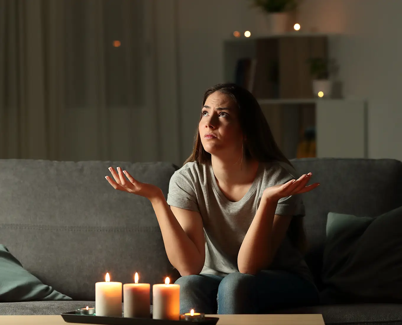 woman sitting in a dark room with candles lit, frustrated that the power has gone out.
