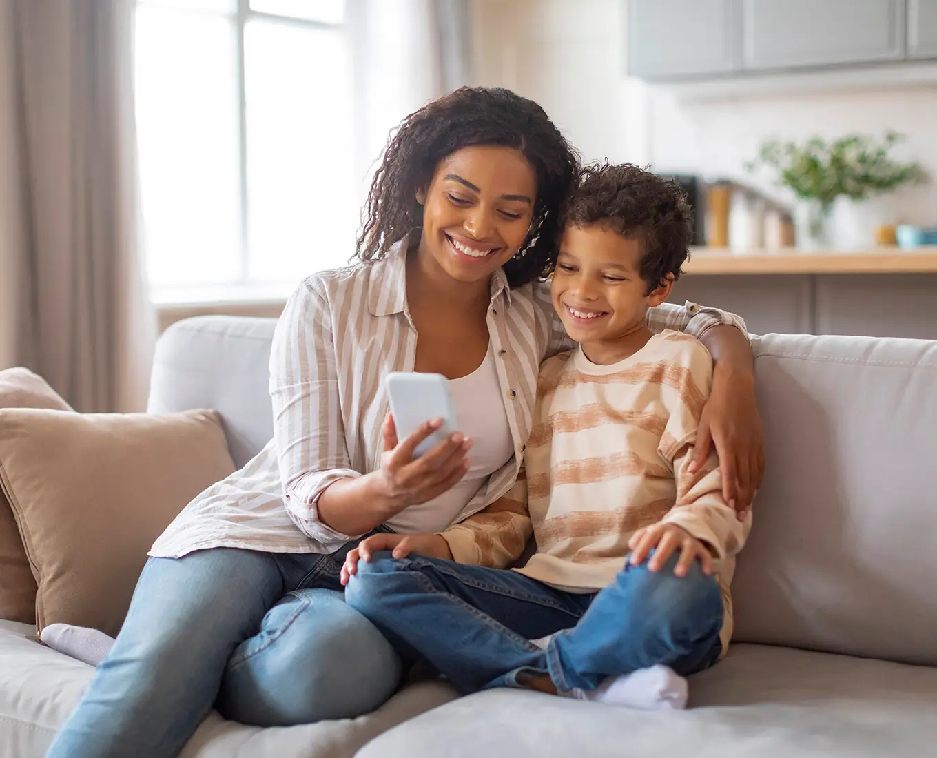 mother and son, wearing long sleeved shirts, are looking at a phone while sitting comfortably on a couch in their living room